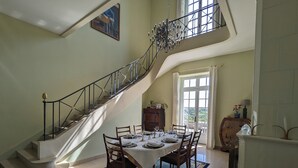 Un comedor con una escalera, una lámpara de araña y vistas al exterior.