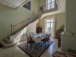 Uma sala de jantar com escada, um candelabro e vista para o exterior.