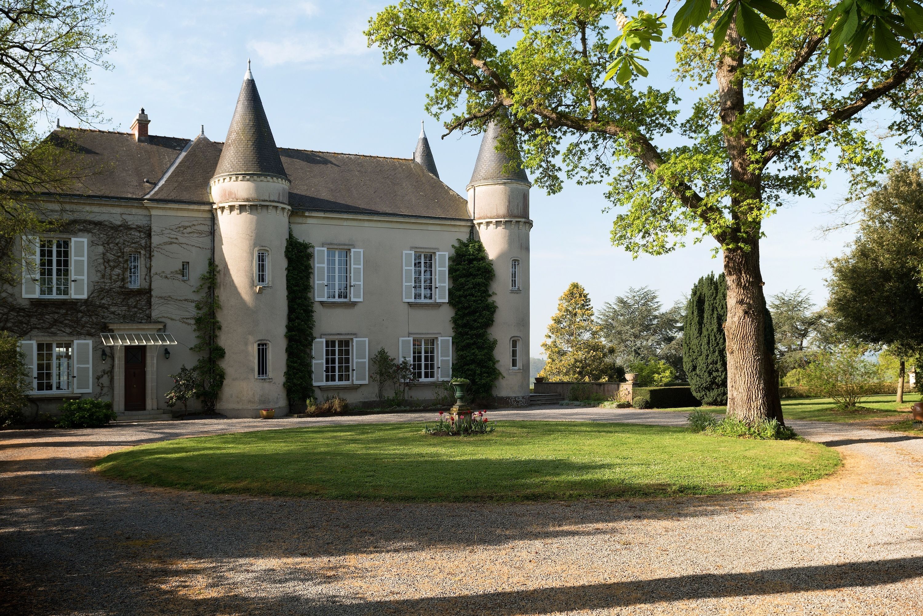 A large, historic building with two prominent towers, a well-maintained lawn, and a gravel driveway.