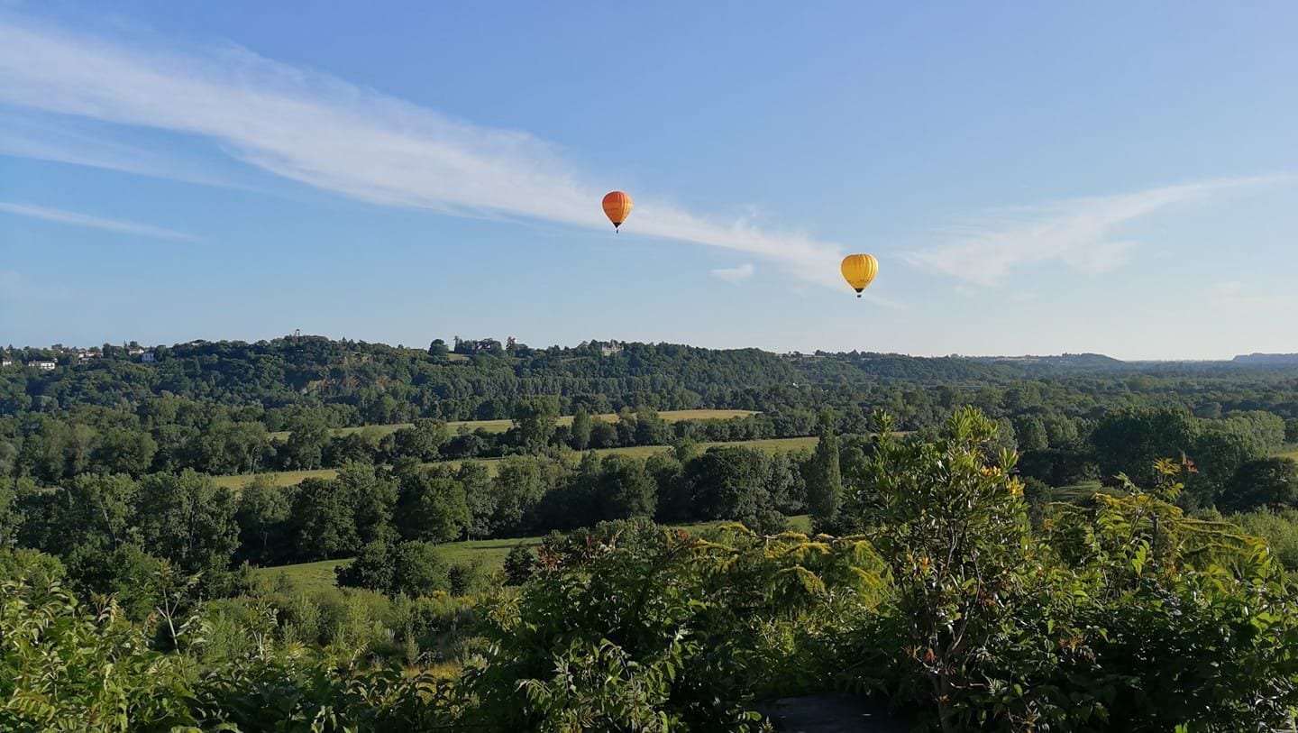 Two hot air balloons flying over a hilly landscape with dense greenery and a clear sky.