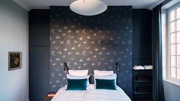 A bedroom with a bed, a wall-mounted shelf, a painting, and a window with curtains.