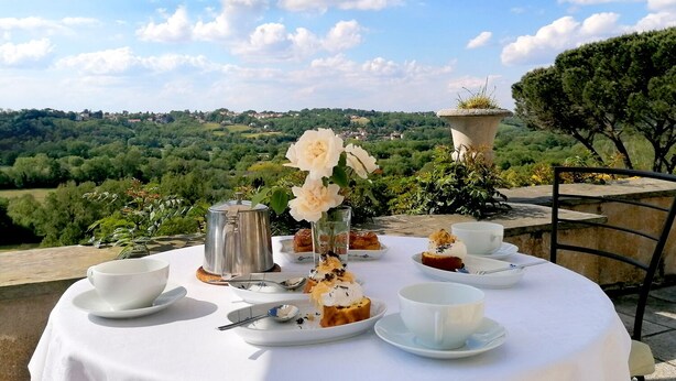 Mesa redonda con mantel blanco, juego de té y pasteles, con vistas a un paisaje pintoresco.