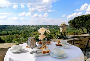 Mesa redonda coberta com toalha branca, serviço de chá e doces, com vista para uma paisagem deslumbrante.
