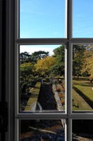 Visão através de uma janela de um jardim com caminho de pedra, árvores e área gramada.