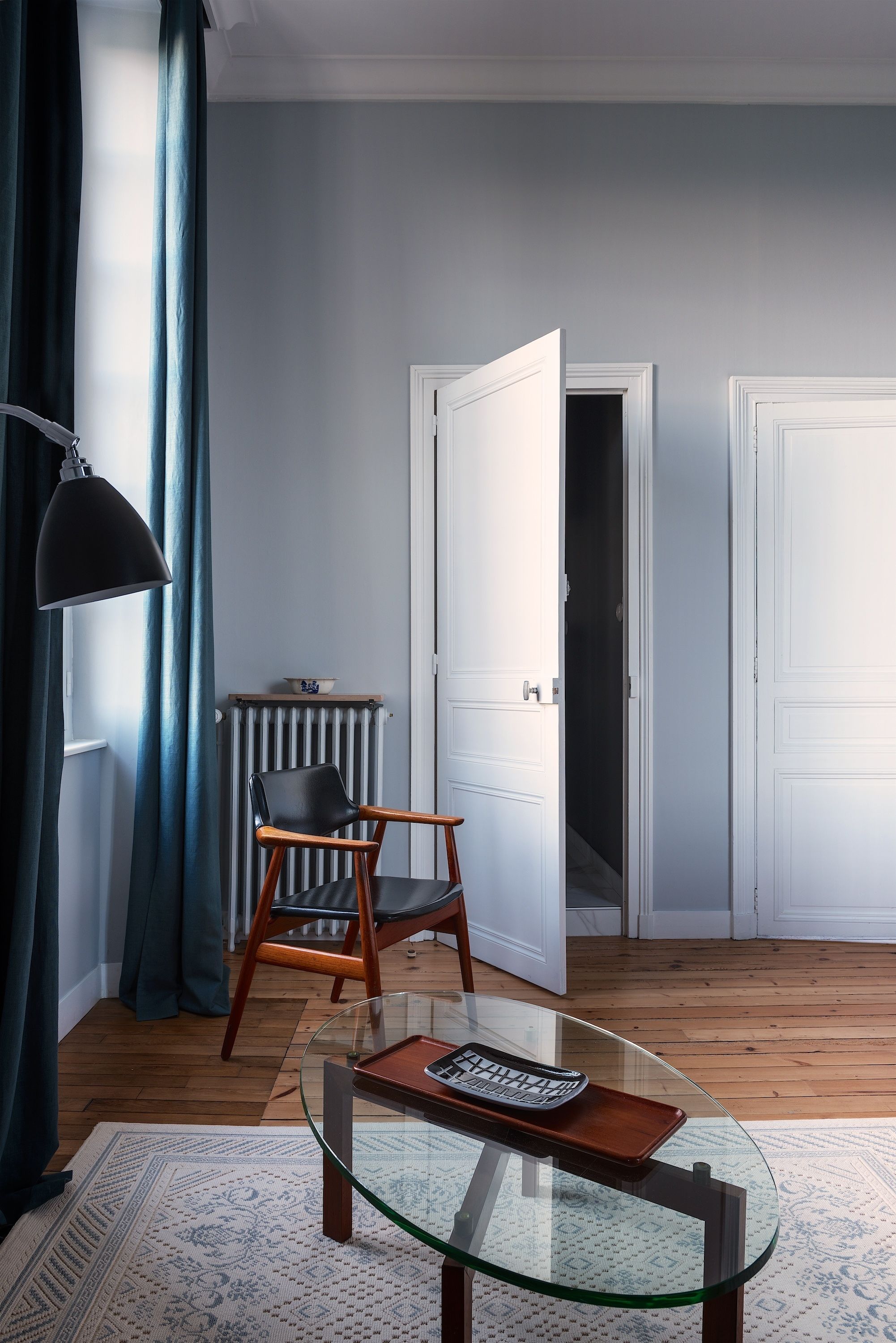 Een kamer met een glazen tafel, een stoel, een radiator en een deur naar een andere kamer.