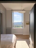 Quarto com uma janela grande, uma cama, um radiador e um guarda-roupa.