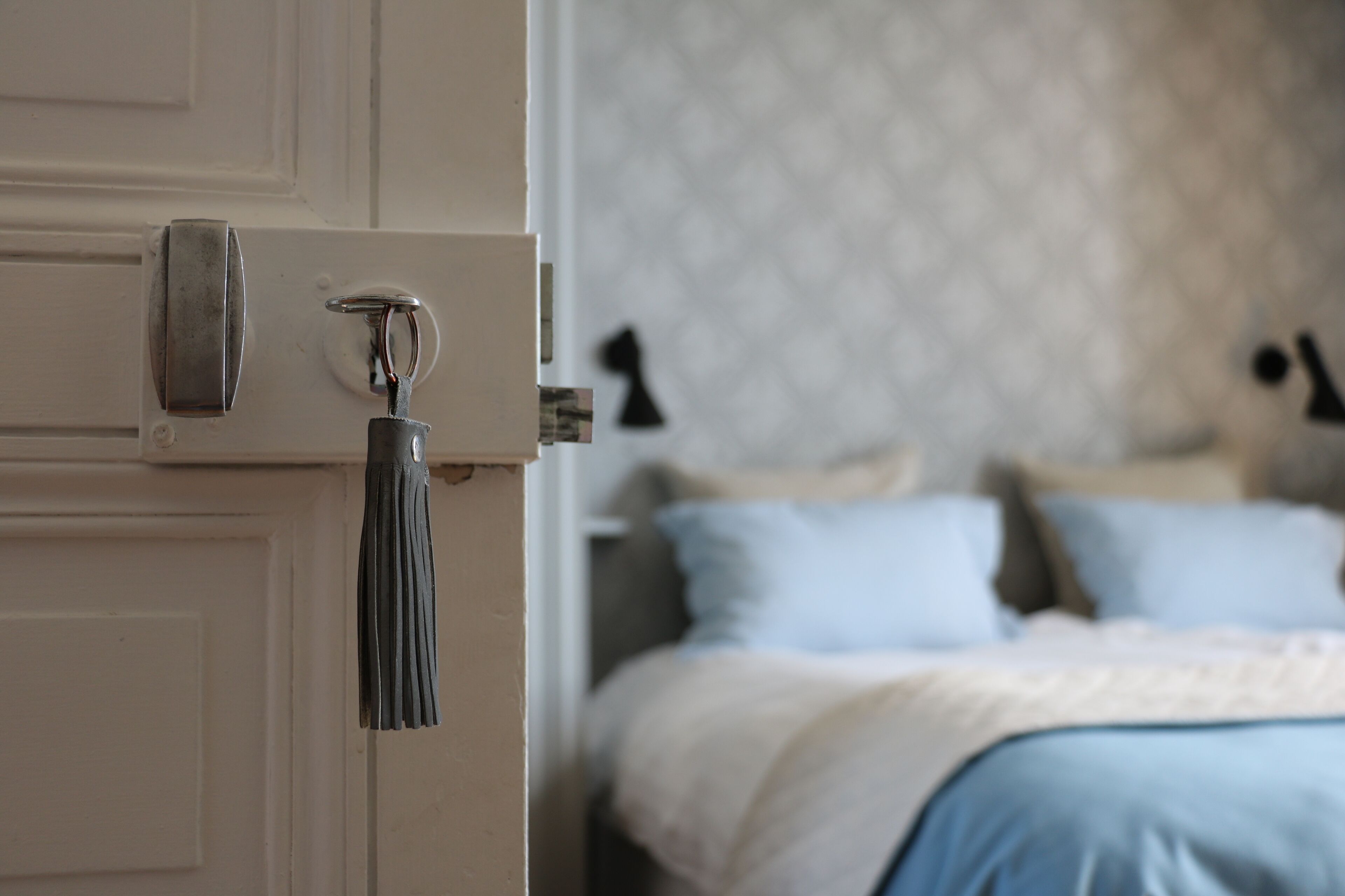 A door with a keyhole and a key, leading to a bedroom with a patterned headboard and a bed with pillows.