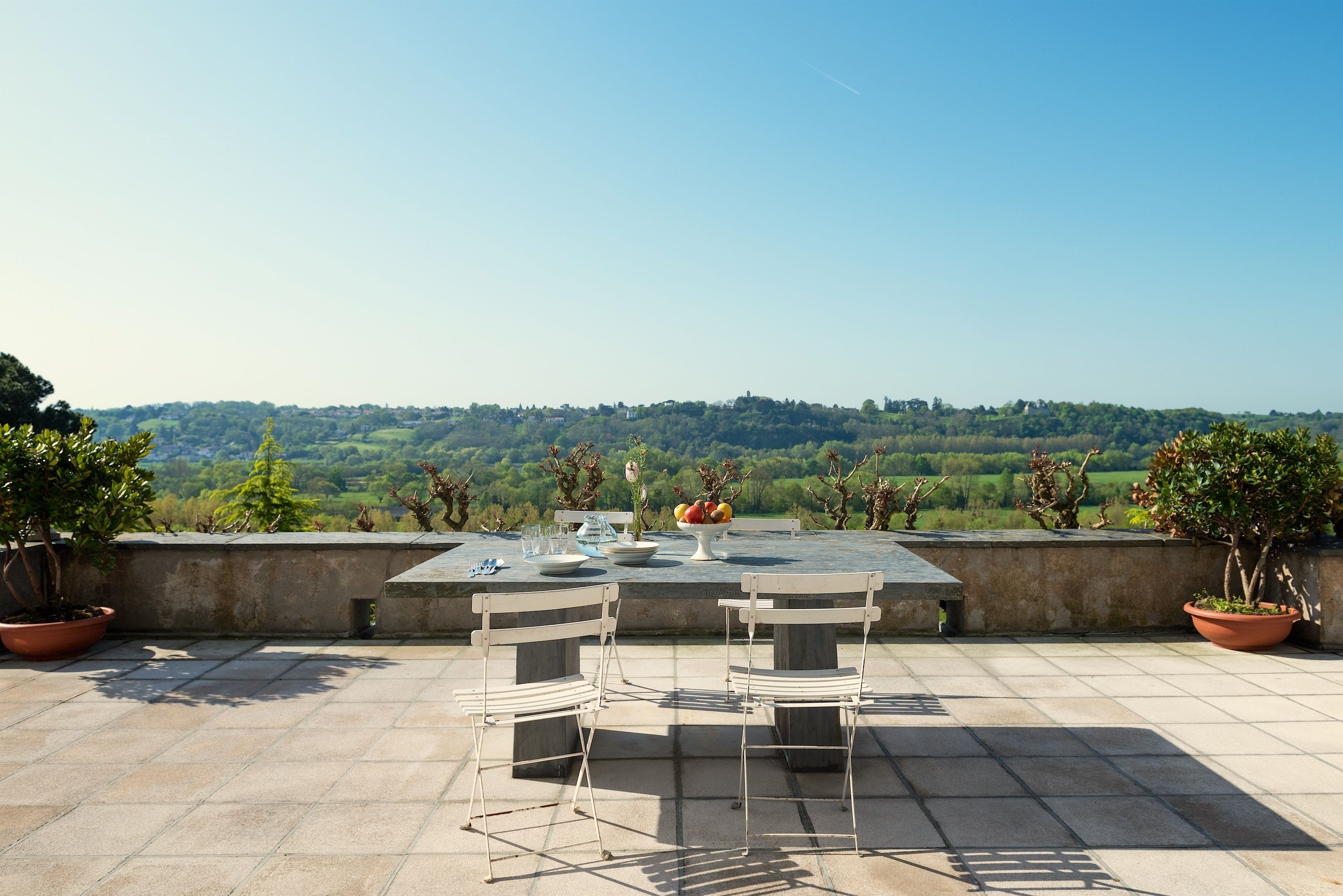 Une terrasse avec une table et des chaises, des plantes en pot et une vue sur un paysage verdoyant.