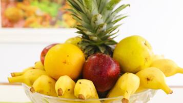 Un saladier en verre rempli de bananes, de pommes et d’un ananas, posé sur une nappe à rayures.