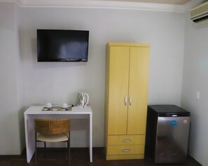 A room with a white desk, a wicker chair, a yellow cabinet, a black television, and a small refrigerator. - Nuevo Hotel (Rivera)