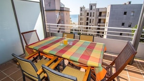 Un balcon avec une table et des chaises, donnant sur un quartier résidentiel avec des immeubles et offrant une vue sur la mer.