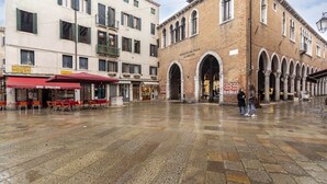 A spacious public square with a historic building featuring arched doorways and a sign reading "Mercato del Pesce". - Residence Le Beccarie - Rialto by Wonderful Italy (Venice)