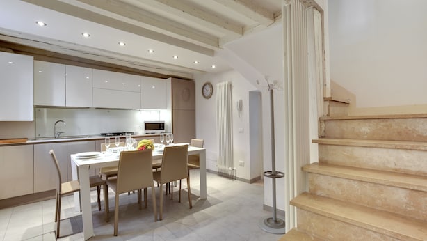A modern kitchen with white cabinets, a dining table set with chairs, and a staircase leading to an upper floor. - San Marco Prestige - S Zaccaria by Wonderful Italy (Venice)