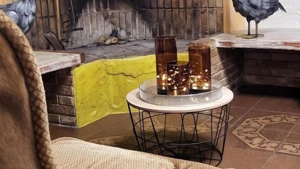 Una sala de estar acogedora con chimenea, una mesa redonda con velas y dos esculturas decorativas de pájaros.