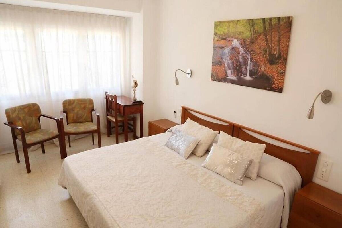 A hotel room with a large bed, two armchairs, a small table, and a painting of a waterfall.