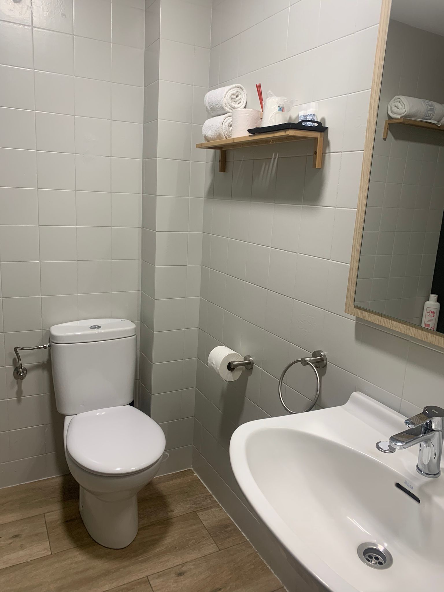 Un baño con inodoro, lavamanos y estante con artículos de aseo.