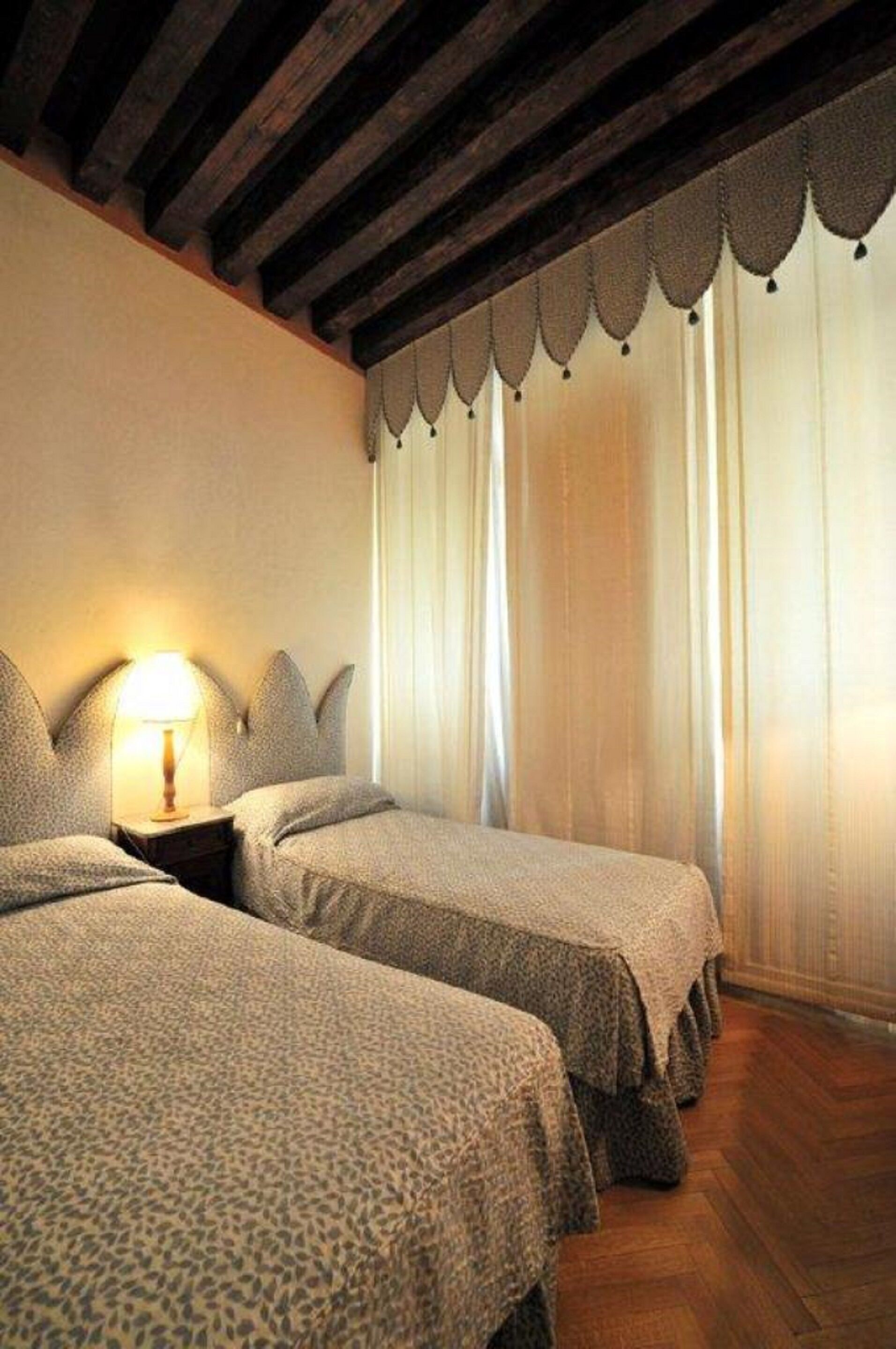Une chambre d’hôtel avec deux lits, un plafond en bois et une fenêtre avec des rideaux.