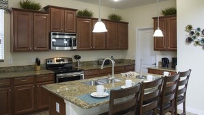 A kitchen with wooden cabinets, granite countertops, stainless steel appliances, and pendant lighting. - Paradise Palms 8950 (Kissimmee)