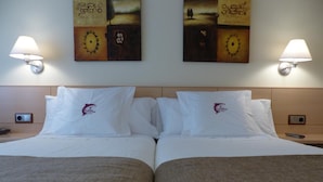 Une chambre d’hôtel avec deux lits, chacun agrémenté d’un oreiller orné d’un logo, une table de chevet avec une télécommande et des lampes fixées au mur.
