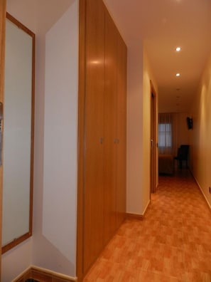 Un passadís amb armaris de fusta, un sòl emblenquinat i una porta que condueix a una altra habitació.