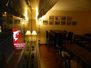 Un restaurant amb un taulell llarg, dues làmpades de taula i quadres amb marc a la paret.