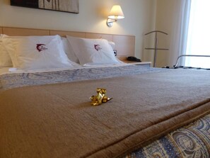 Una habitación de hotel con una cama, almohadas, una lámpara de noche, un teléfono y una pequeña estatua dorada sobre la cama.