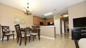 A dining area with a wooden table and chairs, a chandelier, and a kitchen in the background. - Oakwater Resort -2755GOWIS (Kissimmee)
