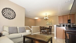 A living room with a sofa, a coffee table, and a dining area with chairs and a chandelier. - Oakwater Resort -2755GOWIS (Kissimmee)