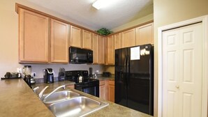 A kitchen with wooden cabinets, a black refrigerator, a microwave, a stove, and a sink. - Oakwater Resort -2755GOWIS (Kissimmee)