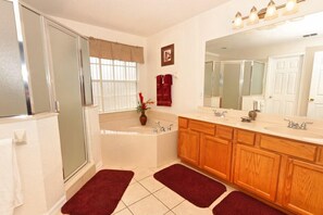A bathroom with a bathtub, a shower, wooden cabinets, a large mirror, and a window with a curtain. - 313 Glen (Davenport)