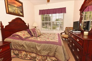 A bedroom with a wooden bed, a dresser, a chair, a desk with a computer, a window with bars, and a painting on the wall. - 313 Glen (Davenport)