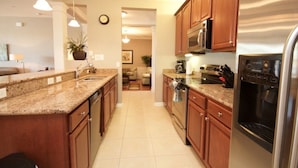 A modern kitchen with granite countertops, wooden cabinets, stainless steel appliances, and pendant lighting. - Lake View Joy (Orlando)