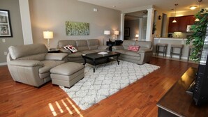 A living room with a sectional sofa, a coffee table, and a rug. There is a kitchen area visible in the background. - Lake View Joy (Orlando)