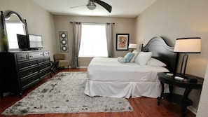 Quarto com cama, cômoda, cadeira e obras de arte na parede.
