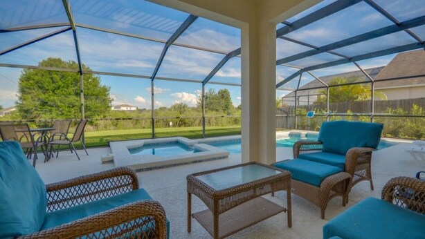 A covered outdoor patio with wicker furniture, a glass table, and a hot tub. - 616BD (Davenport)