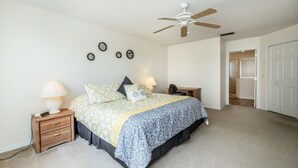 Une chambre à coucher comprenant un lit, des tables de chevet, un ventilateur de plafond et une porte donnant sur une autre pièce.