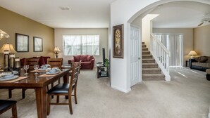 Un vaste salon comprenant un coin repas, un escalier et une porte donnant sur une autre pièce.