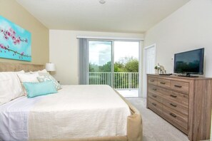 A bedroom with a bed, a dresser, a television, and a balcony with a view of greenery.