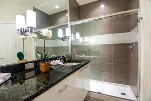 A modern bathroom with a granite countertop, a sink, a mirror, and a glass shower enclosure.