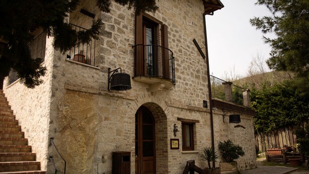 A stone building with a wooden door, a balcony, and a staircase leading to the entrance. - Al Regio Tratturo (Manoppello)