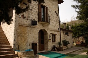 A stone building with a wooden door, a balcony, and a staircase leading to the entrance.