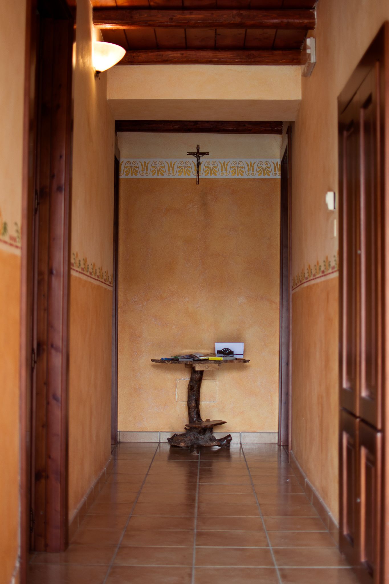 A hallway with a wooden door frame, a small table with a cross, and a wall with a decorative border.