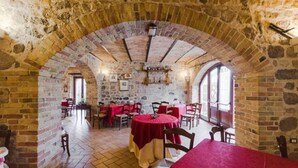 An interior with stone walls, a high arched ceiling, and tables with red tablecloths. - Al Regio Tratturo (Manoppello)