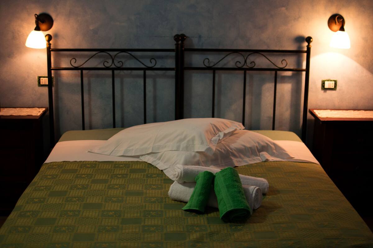 A neatly made bed with a green patterned bedspread, white pillows, and green towels on a metal headboard.