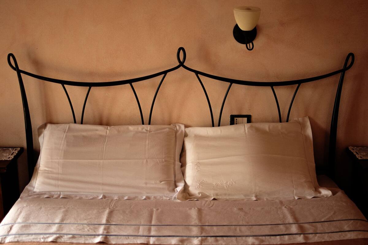A bed with a metal headboard, two pillows, and a bedside table with a lamp.