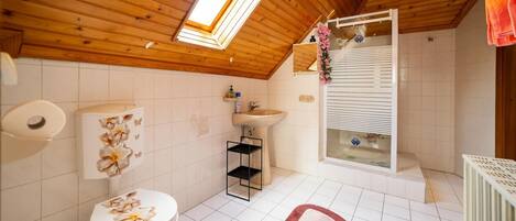 Ett badrum med ett träpanelat tak, ett takfönster, en toalett dekorerad med blommor, ett handfat och en duschhörna.