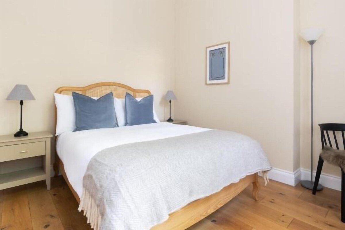 Een enkel bed met houten frame, twee nachtkastjes met lampen, een stoel en een foto aan de muur.