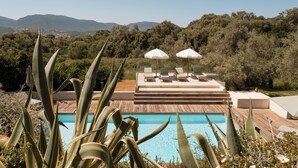 A pool with a wooden deck, surrounded by cacti and a view of hills. - L'Hostellerie Du Moulin Des Oliviers (Olmeto)