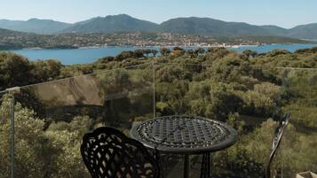 Varanda com mesa e cadeiras com vista para a paisagem costeira e montanhas ao longe.