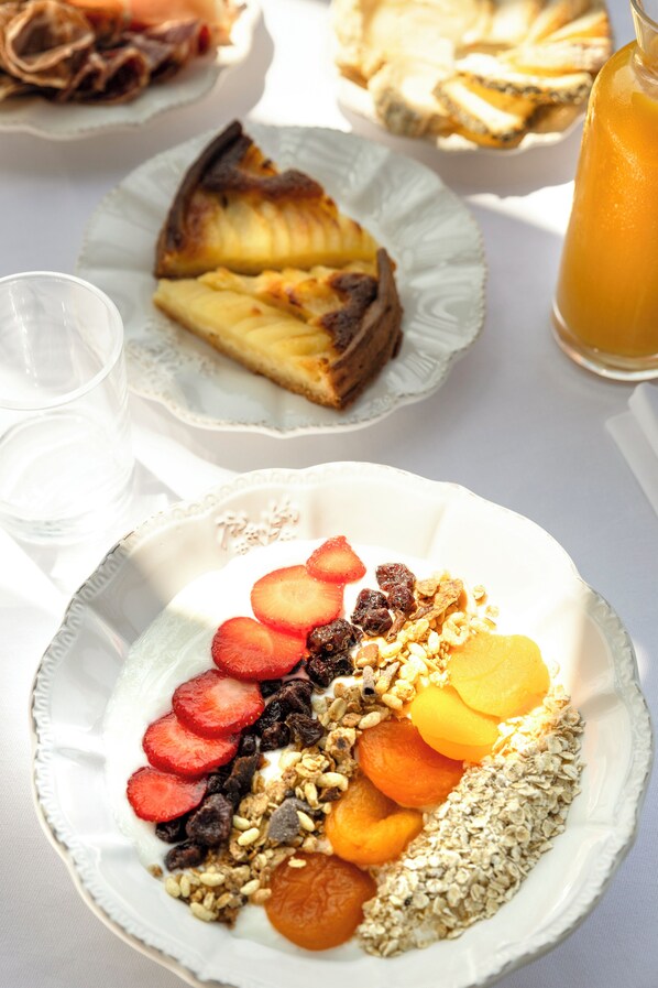 A breakfast setting with plates of food, including a fruit and granola mix, a slice of pie, and a glass of orange juice. - L'Hostellerie Du Moulin Des Oliviers (Olmeto)